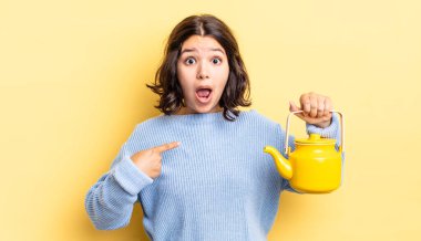 Genç İspanyol kadın şok olmuş ve ağzı açık, kendini işaret ederek şaşırmış görünüyor. çaydanlık konsepti