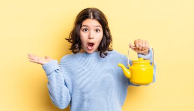 Genç İspanyol kadın şaşırmış ve şok olmuş görünüyor. Çenesi düşmüş ve elinde bir nesne tutuyor. çaydanlık konsepti