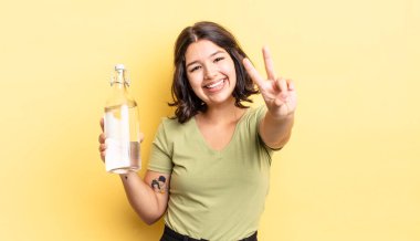 Genç İspanyol kadın gülümsüyor ve mutlu görünüyor, zafer ya da barış işareti yapıyor. su şişesi kavramı