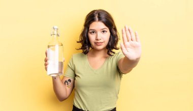 Genç İspanyol kadın ciddi görünüyor. Avuç içini gösteriyor. Durdurma hareketi yapıyor. su şişesi kavramı