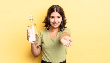 Genç İspanyol kadın mutlu bir şekilde gülümsüyor ve bir konsept sunuyor. su şişesi kavramı