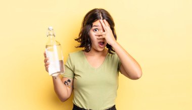 Genç İspanyol bir kadın şok olmuş, korkmuş ya da korkmuş görünüyor. Yüzü elle kapatılmış. su şişesi kavramı