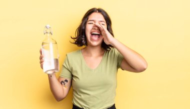 Genç İspanyol kadın kendini mutlu hissediyor, elleri ağzının kenarında bağırıyor. su şişesi kavramı