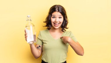 Genç İspanyol kadın kendini mutlu hissediyor ve heyecanla kendini işaret ediyor. su şişesi kavramı