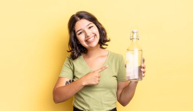 Genç İspanyol kadın neşeyle gülümsüyor, mutlu hissediyor ve bir tarafı işaret ediyor. su şişesi kavramı