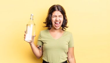 Genç İspanyol kadın agresif bir şekilde bağırıyor, çok kızgın görünüyor. su şişesi kavramı