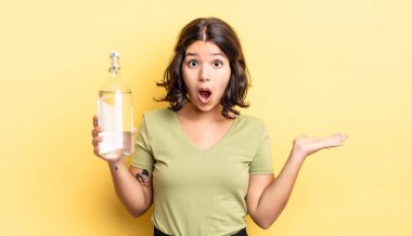 Genç İspanyol kadın şaşırmış ve şok olmuş görünüyor. Çenesi düşmüş ve elinde bir nesne tutuyor. su şişesi kavramı