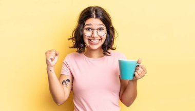 Genç İspanyol kadın şokta, gülüyor ve başarıyı kutluyor. kahve fincanı konsepti