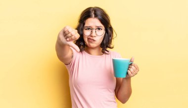 Latin kökenli genç bir kadın kızmış, baş parmağını kaldırmış. kahve fincanı konsepti