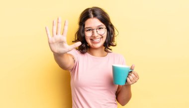 Genç İspanyol kadın gülümsüyor ve arkadaş canlısı görünüyor, beş numarayı gösteriyor. kahve fincanı konsepti