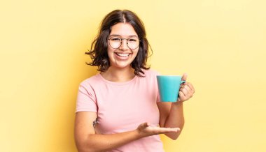 Genç İspanyol kadın neşeyle gülümsüyor, mutlu hissediyor ve bir konsept gösteriyor. kahve fincanı konsepti