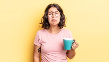 Genç İspanyol kadın üzgün ve mızmızlanıyor. Mutsuz bir bakışı var ve ağlıyor. kahve fincanı konsepti