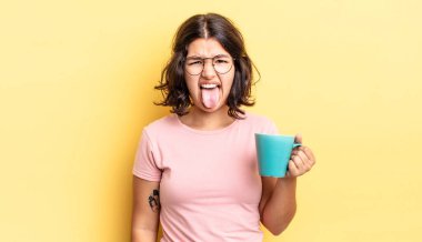 Genç İspanyol kadın iğreniyor, sinirleniyor ve dili dışarı çıkıyor. kahve fincanı konsepti