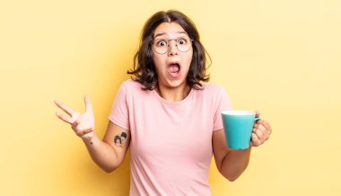 Genç İspanyol kadın şok olmuş ve şaşırmış hissediyor. kahve fincanı konsepti