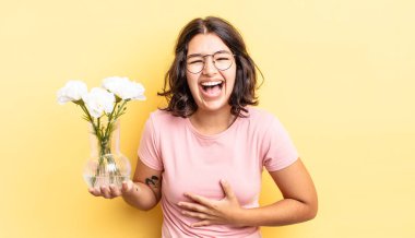 Genç İspanyol kadın komik bir şakaya yüksek sesle gülüyor. çiçek saksı konsepti