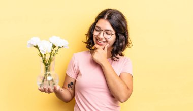Genç İspanyol kadın mutlu ve kendinden emin bir ifadeyle gülümsüyor. Elleri çenesinde. çiçek saksı konsepti
