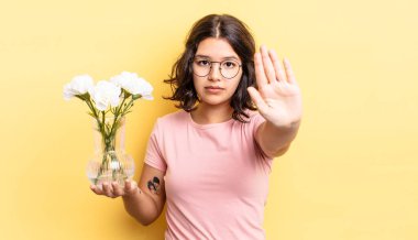Genç İspanyol kadın ciddi görünüyor. Avuç içini gösteriyor. Durdurma hareketi yapıyor. çiçek saksı konsepti