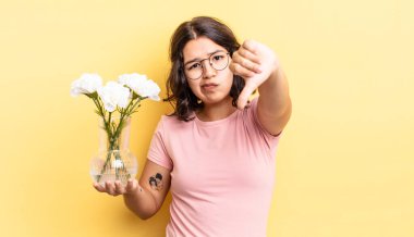 Latin kökenli genç bir kadın kızmış, baş parmağını kaldırmış. çiçek saksı konsepti