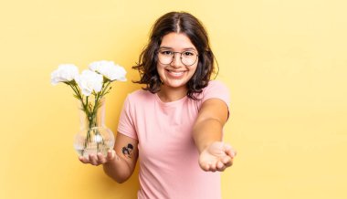 Genç İspanyol kadın mutlu bir şekilde gülümsüyor ve bir konsept sunuyor. çiçek saksı konsepti