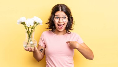 Genç İspanyol kadın kendini mutlu hissediyor ve heyecanla kendini işaret ediyor. çiçek saksı konsepti