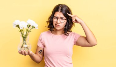 Genç İspanyol kadın şaşkın ve şaşkın hissediyor, senin deli olduğunu gösteriyor. çiçek saksı konsepti