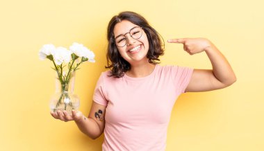 Genç İspanyol kadın kendine güvenerek gülümsüyor ve kendi gülüşünü gösteriyor. çiçek saksı konsepti