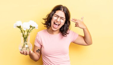 Genç İspanyol kadın mutsuz ve stresli görünüyor, intihar jesti silah işareti yapıyor. çiçek saksı konsepti