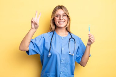 Güzel sarışın kız gülümsüyor ve arkadaş canlısı görünüyor. İki numarayı gösteriyor. hemşire bir aşı konsepti