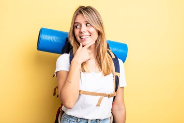 Güzel sarışın kız gülümsüyor mutlu, kendine güvenen bir yüz ifadesi ve elleri çenesinde. Yürüyüş konsepti