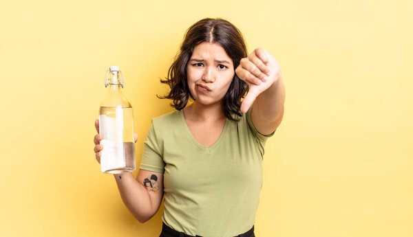 young hispanic woman feeling cross,showing thumbs down. water bottle concept