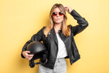 Güzel sarışın kız şaşkın ve kafası karışık, kaşınan bir kafa hissediyor. Motosiklet kaskı konsepti