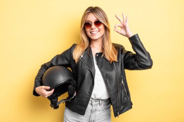 Güzel sarışın kız kendini mutlu hissediyor, iyi bir jestle onaylıyor. Motosiklet kaskı konsepti