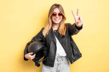 Güzel sarışın kız gülümsüyor ve mutlu görünüyor, zafer ya da barış işareti yapıyor. Motosiklet kaskı konsepti