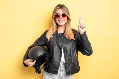 Güzel sarışın kız gülümsüyor ve arkadaş canlısı görünüyor. Bir numarayı gösteriyor. Motosiklet kaskı konsepti