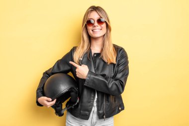 Güzel sarışın kız neşeyle gülümsüyor, mutlu hissediyor ve bir tarafı işaret ediyor. Motosiklet kaskı konsepti