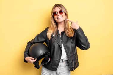 Güzel sarışın kız kendi gülüşünü göstererek kendine güvenerek gülümsüyor. Motosiklet kaskı konsepti