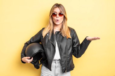 Güzel sarışın kız şaşırmış ve şok olmuş görünüyor. Çenesi düşmüş ve elinde bir nesne var. Motosiklet kaskı konsepti