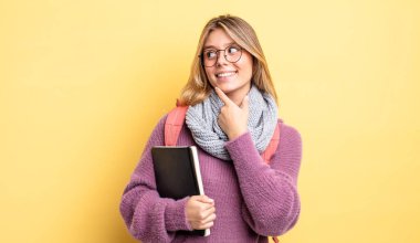 Güzel sarışın kız gülümsüyor mutlu, kendine güvenen bir yüz ifadesi ve elleri çenesinde. öğrenci konsepti