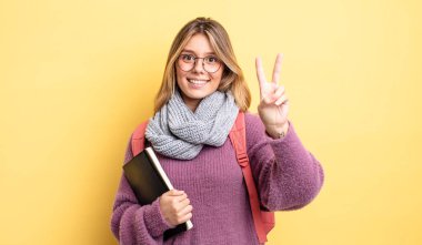 Güzel sarışın kız gülümsüyor ve mutlu görünüyor, zafer ya da barış işareti yapıyor. öğrenci konsepti