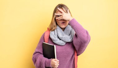 Güzel sarışın kız şok olmuş, korkmuş ya da korkmuş görünüyor. Yüzü elle kapatılmış. öğrenci konsepti