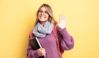 Güzel sarışın kız mutlu bir şekilde gülümsüyor, el sallıyor, hoş geldin diyor ve seni selamlıyor. öğrenci konsepti