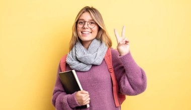 Güzel sarışın kız gülümsüyor ve arkadaş canlısı görünüyor. İki numarayı gösteriyor. öğrenci konsepti