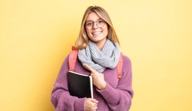 Güzel sarışın kız neşeyle gülümsüyor, mutlu hissediyor ve bir tarafı işaret ediyor. öğrenci konsepti