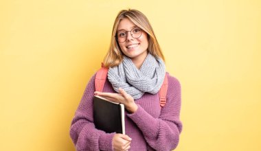 Güzel sarışın kız neşeyle gülümsüyor, mutlu hissediyor ve bir konsept gösteriyor. öğrenci konsepti