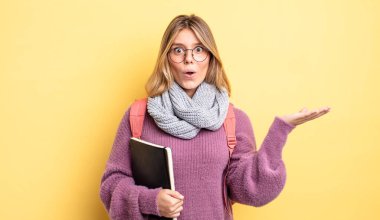 Güzel sarışın kız şaşırmış ve şok olmuş görünüyor. Çenesi düşmüş ve elinde bir nesne var. öğrenci konsepti