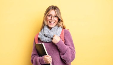 Güzel sarışın kız kendini mutlu hissediyor ve bir meydan okumayla yüzleşiyor ya da kutluyor. öğrenci konsepti