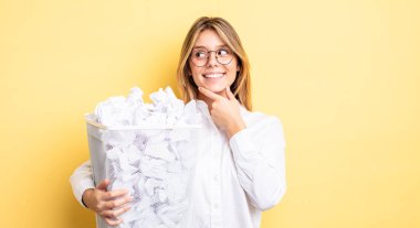 Güzel sarışın kız gülümsüyor mutlu, kendine güvenen bir yüz ifadesi ve elleri çenesinde. kağıt toplar çöp konsepti