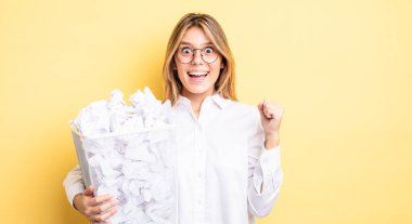 Güzel sarışın kız şokta, gülüyor ve başarıyı kutluyor. kağıt toplar çöp konsepti