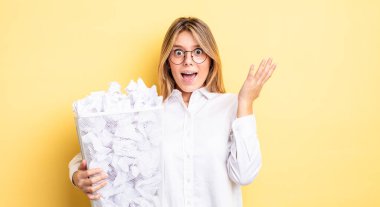 Güzel sarışın kız kendini mutlu hissediyor ve inanılmaz bir şeye hayret ediyor. kağıt toplar çöp konsepti