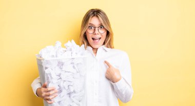 Güzel sarışın kız mutlu hissediyor ve heyecanla kendini işaret ediyor. kağıt toplar çöp konsepti